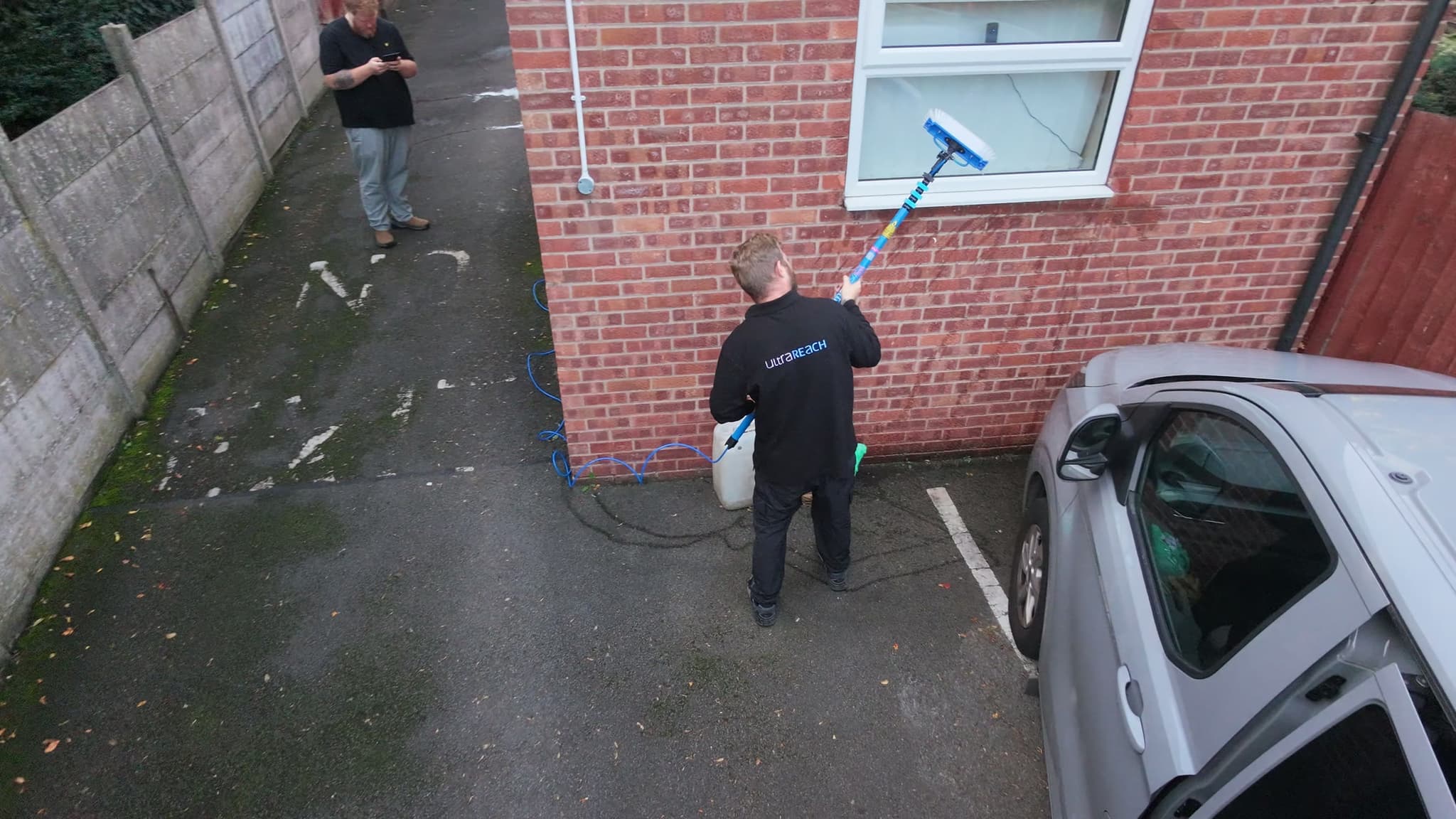 Seen from above: a window cleaner in an UltraReach jacket cleaning a window with an UltraReach water fed pole and brush.